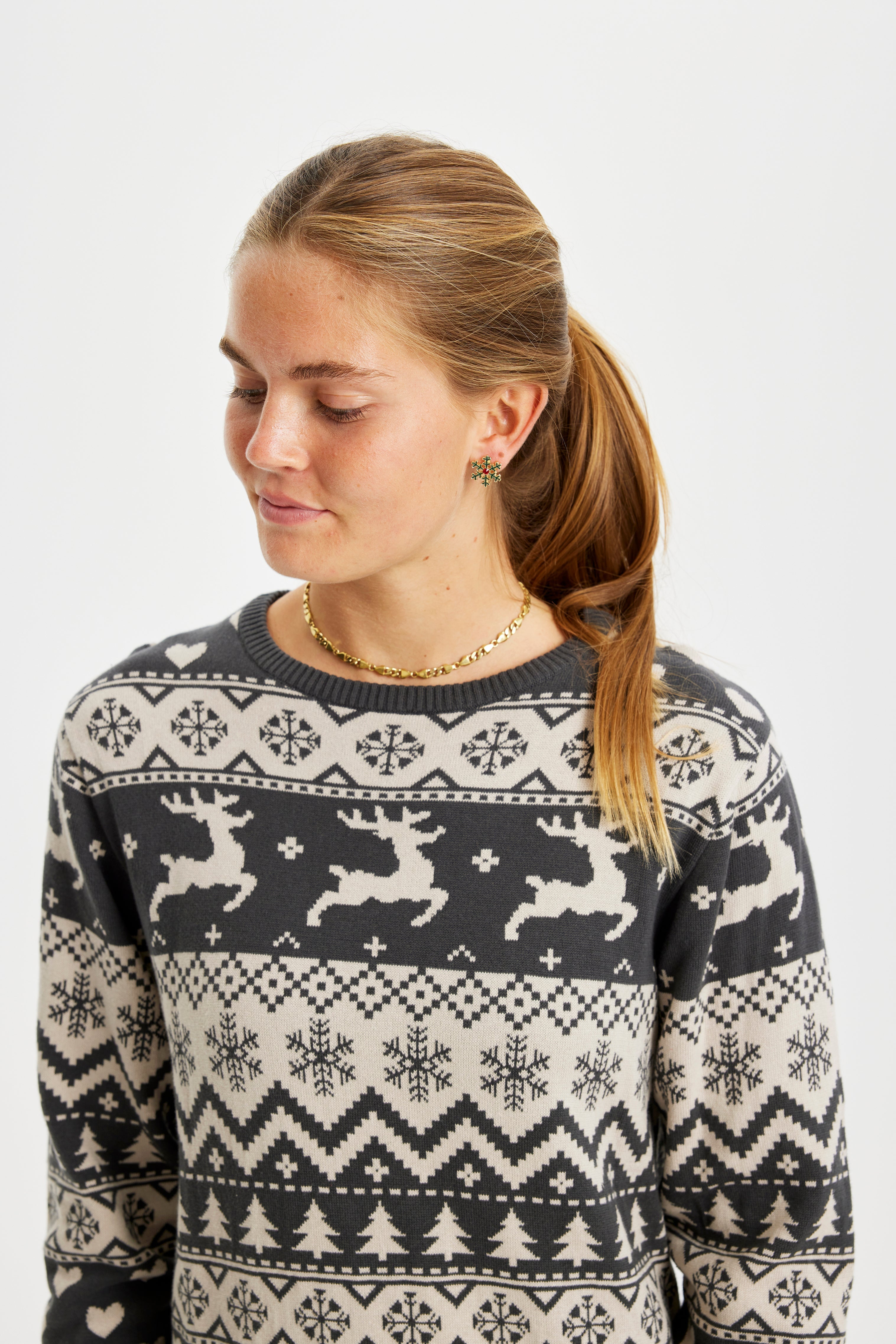 Eine zur Seite blickende Frau in einem grauen Weihnachtskleid mit Rentieren darauf.